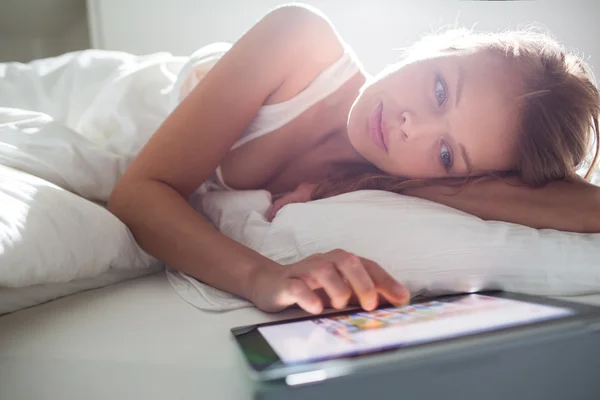 Ładna, młoda kobieta za pomocą tabletu komputera w łóżku — Zdjęcie stockowe