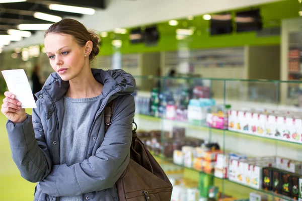 Mujer joven que busca las píldoras adecuadas en una farmacia moderna — Foto de Stock