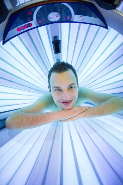 Bello giovane uomo che si rilassa durante una sessione di abbronzatura in un solarium — Foto Stock