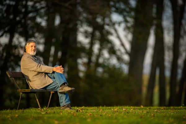 Portrait of a senior man outdoors, sitting on a bench in a park — Stock Photo, Image