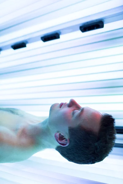 Joven guapo relajándose durante una sesión de bronceado en un solarium — Foto de Stock