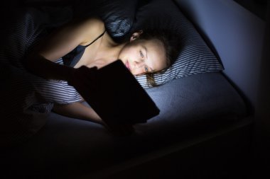 Gece geç saatlerde onun yatağında tablet bilgisayarını kullanan genç kadın