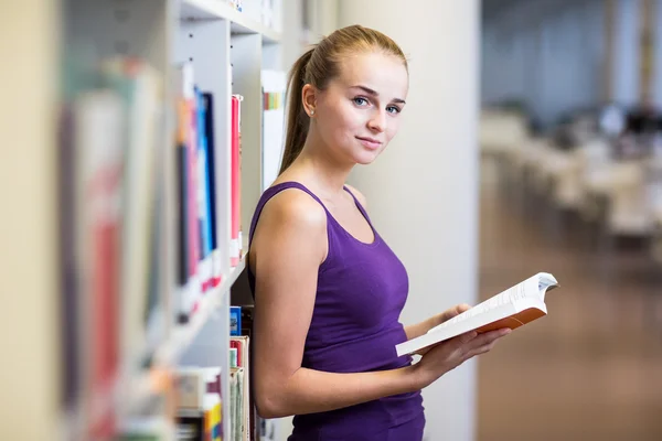 Vacker, kvinnlig collegestudent i ett bibliotek, letar du efter en bok — Stockfoto