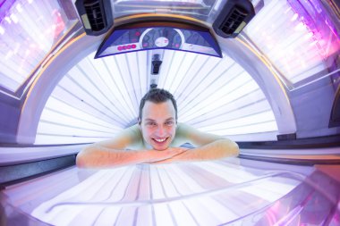 Handsome young man relaxing during a tanning session in a solarium clipart