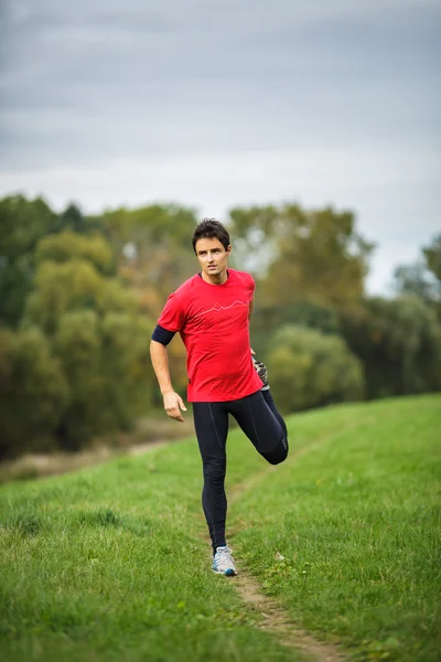 Joven hombre estirando sus piernas antes de su carrera diaria — Foto de Stock