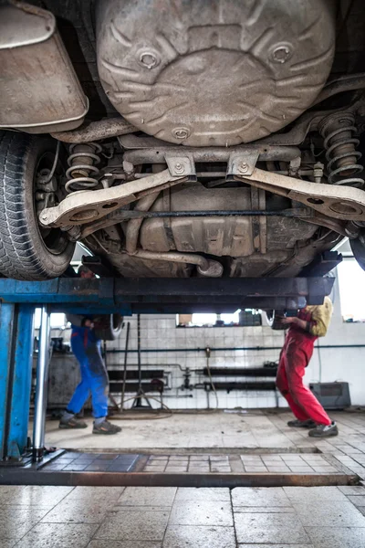 Dentro de un garaje - dos mecánicos trabajando en un coche, cambiando de rueda — Foto de Stock