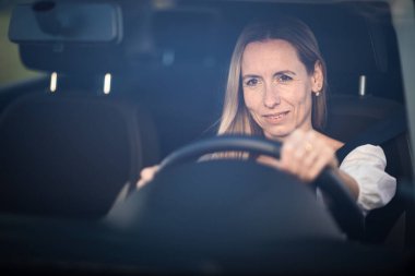 Arabasının direksiyonunda orta yaşlı güzel bir kadın.