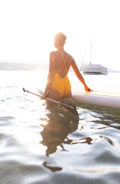 Kürek çekme konsepti - Güzel, genç bir kadın sıcak öğleden sonra ışığında güzel bir gölde kürek çekiyor