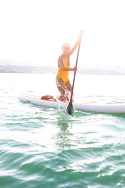 Kürek çekme konsepti - Güzel, genç bir kadın sıcak öğleden sonra ışığında güzel bir gölde kürek çekiyor
