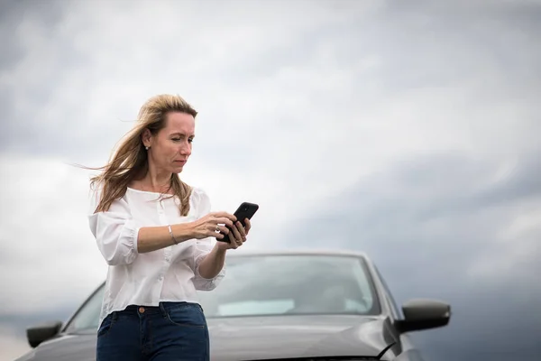 Pretty middle aged woman having car troubles - broken down car on the side of the road, calling the insurance company for assistance