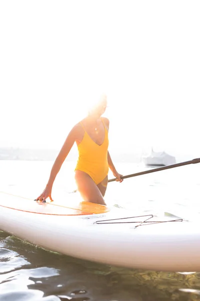 SUP Stand up paddle board concept - Pretty, young woman paddle boarding on a lovely lake in warm late afternoon light