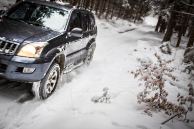 Hareket, karla kaplı orman yolunda hızla giden büyük bir SUV 'un görüntüsünü bulanıklaştırdı.