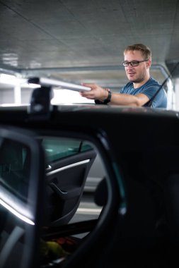 Yakışıklı genç sürücü bisiklete binmeye hazırlanıyor. Arabasının çatısına bir bisiklet parkı koyuyor.