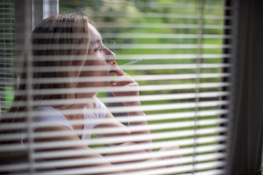 Evde sigara yakan orta yaşlı bir kadın, günlük nikotin dozunu alıyor, sağlıksız alışkanlığına karşı koyamıyor.