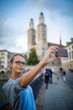 İsviçre, Zürih 'teki Grossmunster Kilisesi önünde selfie çeken güzel bir bayan turist.