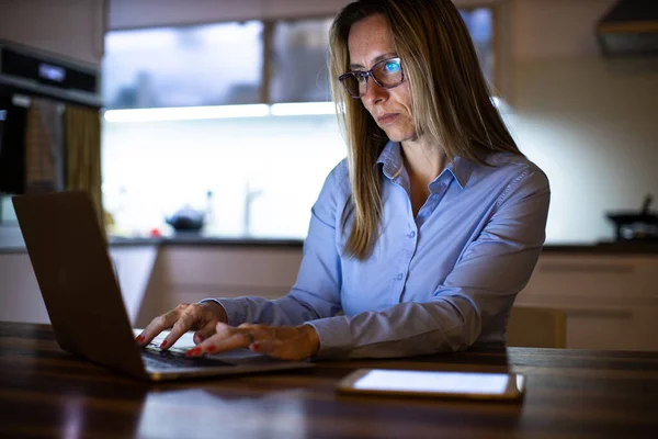 Pretty, middle-aged woman working late in the day on a laptop computer at home, running a business from home, working remotely - getting frustrated