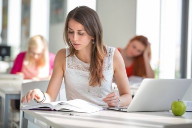 Kütüphanedeki güzel genç üniversite öğrencisi (sığ DOF; renk tonlu resim)