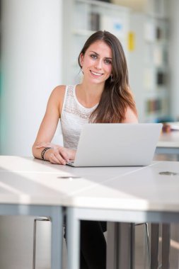 Kütüphanedeki güzel genç üniversite öğrencisi (sığ DOF; renk tonlu resim)