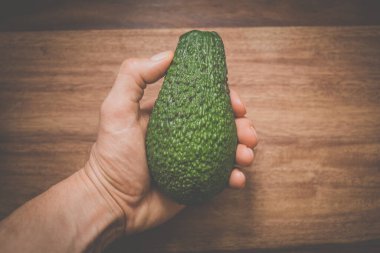 Avokado tutan bir elin yakın çekimi. Yerel kaynaklı, organik gıda.