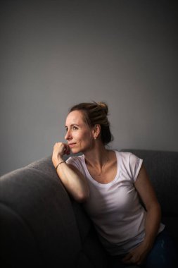 Evde kendini üzgün, yalnız ve endişeli hisseden orta yaşlı bir kadın var.)