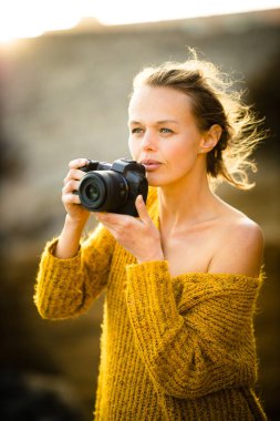 Hobi fotoğrafçısı konsepti. Açık havada genç bir kadının sıcak akşam güneşinde aynasız kamerasıyla fotoğraf çekerken çekilmiş bir fotoğrafı.