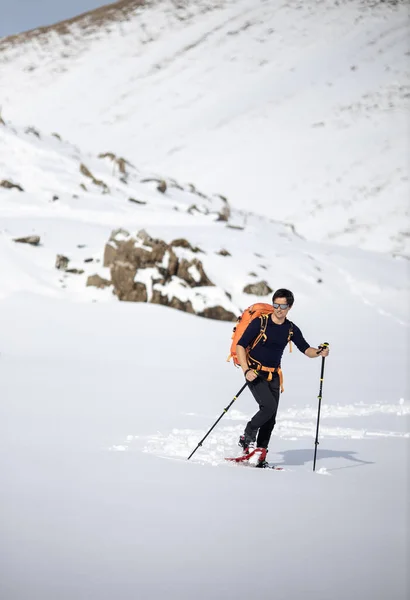 冬のスポーツ 多くの雪で覆われた高い山の中でスノーシューで歩く若い男 背景の山に選択的な焦点 — ストック写真