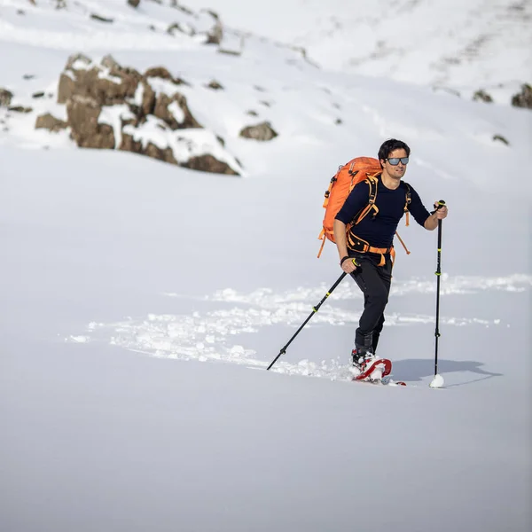 冬のスポーツ 多くの雪で覆われた高い山の中でスノーシューで歩く若い男 背景の山に選択的な焦点 — ストック写真