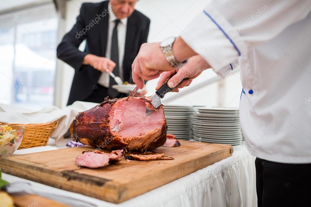 Catering service employee cutting ham