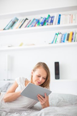 Genç kadın yatakta, tablet bilgisayarını kullanarak
