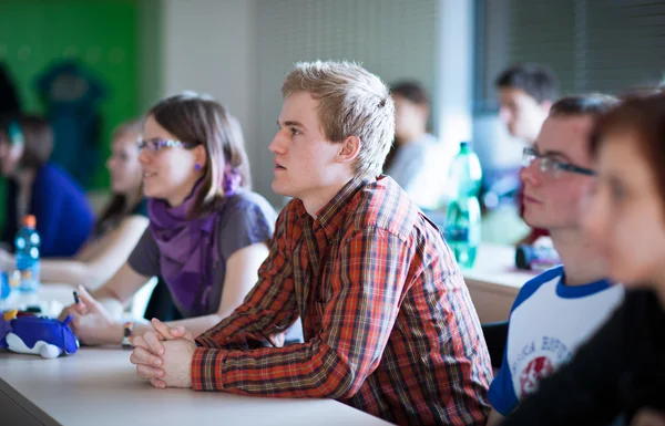 Knappe college student zitten in een klaslokaal vol met studenten — Stockfoto