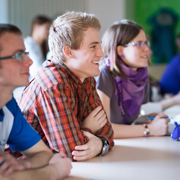 Knappe college student zitten in een klaslokaal vol met studenten — Stockfoto