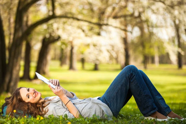 Jovem mulher usando seu computador tablet enquanto relaxa ao ar livre — Fotografia de Stock