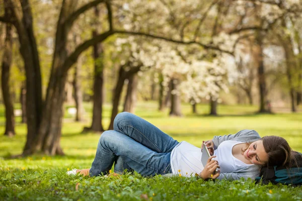 Jonge vrouw met behulp van haar tablet-pc terwijl u ontspant buitenshuis — Stockfoto