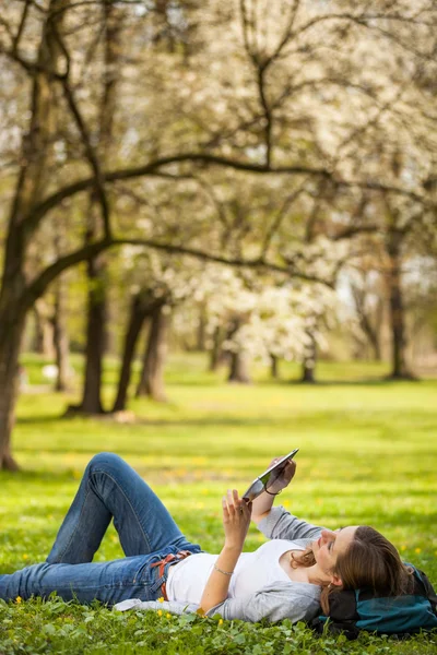 Tânără femeie folosind computerul ei tabletă în timp ce se relaxează în aer liber — Fotografie, imagine de stoc