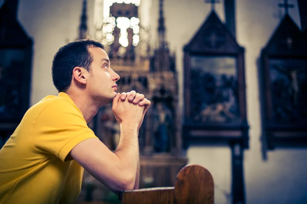 En stilig ung man som ber i en kyrka — Stockfoto