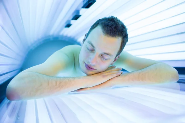 Bonito jovem relaxante durante uma sessão de bronzeamento — Fotografia de Stock