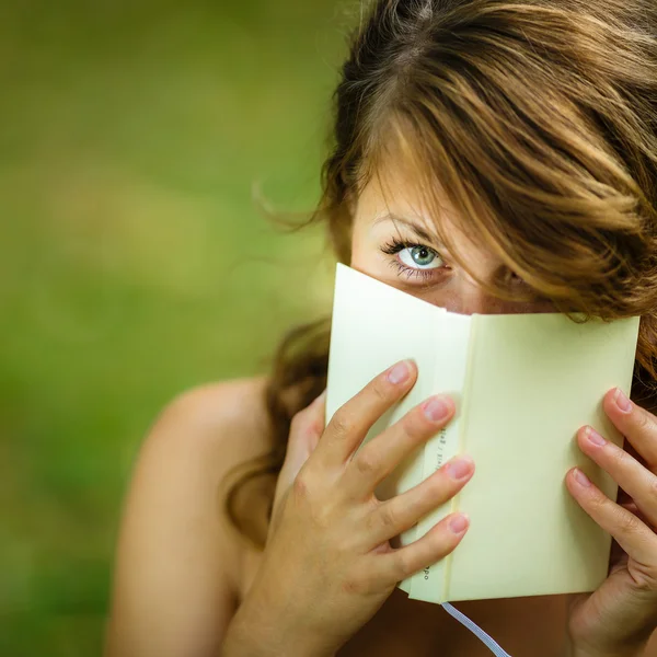 Linda joven que cubre su cara con un libro que está leyendo — Foto de Stock