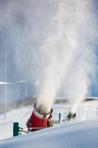 Snow-machine bursting artificial snow  over a skiing slope