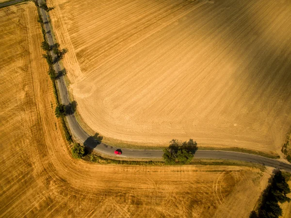 Εναέρια άποψη του δρόμου μια χώρα ανάμεσα σε πεδία με ένα κόκκινο αυτοκίνητο — Φωτογραφία Αρχείου
