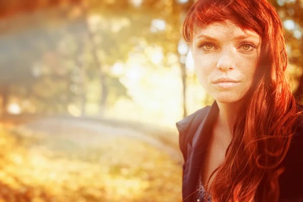 Woman with freckles and red long hair in fall park Royalty Free Stock Images