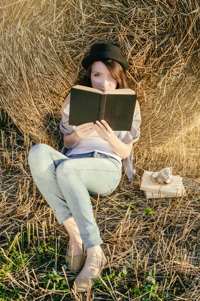 Girll hipster reads book against hay bale in fall — Stock Photo, Image