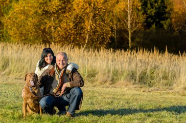 Cheerful couple with dog in autumn countryside clipart