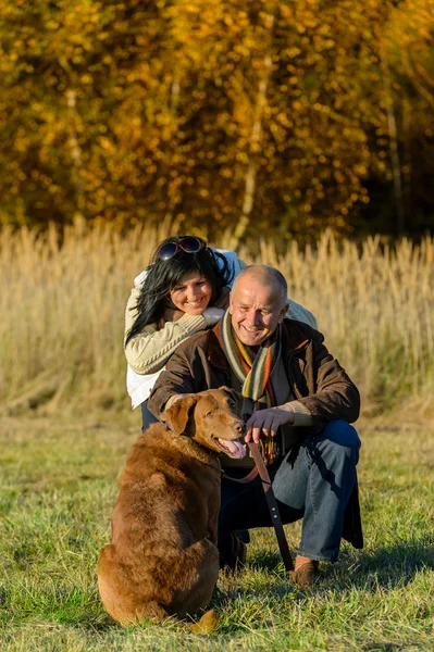 Casal alegre com cão no campo de outono — Fotografia de Stock