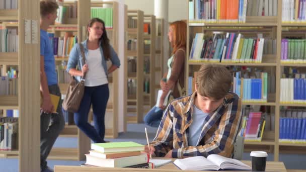 Sorrindo estudante menino aprendendo por mesa na biblioteca da faculdade — Vídeo de Stock