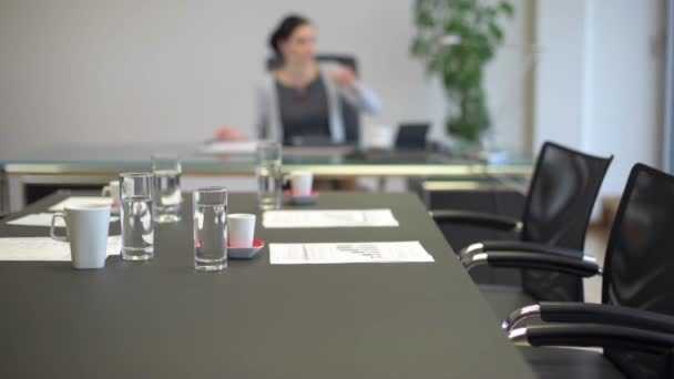 Mesa de la sala de reuniones de oficina con mujer de negocios borrosa en segundo plano — Vídeo de stock