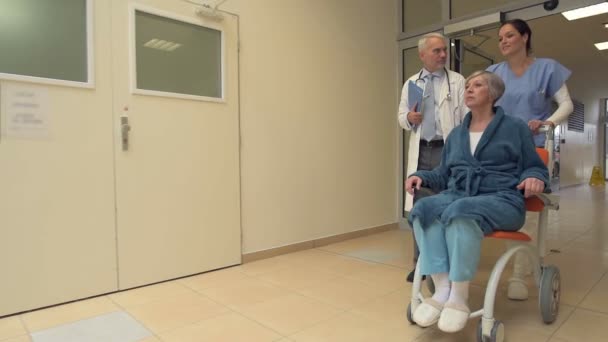 Doktor ve hemşire hasta hastanede tekerlekli sandalyede iterek — Stok video