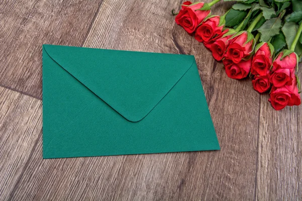 Envelope verde e rosas em um fundo de madeira — Fotografia de Stock