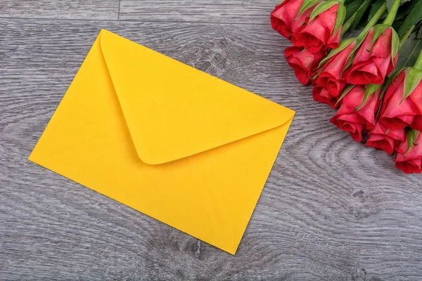 Gelber Umschlag und Rosen auf einem hölzernen Hintergrund — Stockfoto