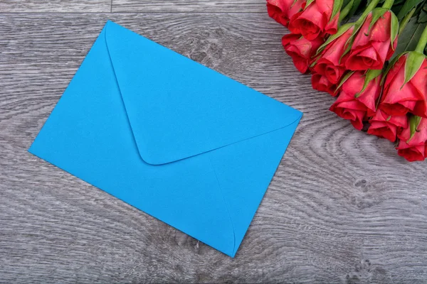 Envelope azul e rosas em um fundo de madeira — Fotografia de Stock