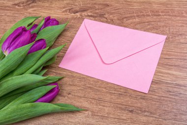 Pembe zarf ve ahşap arka plan üzerinde mor laleler